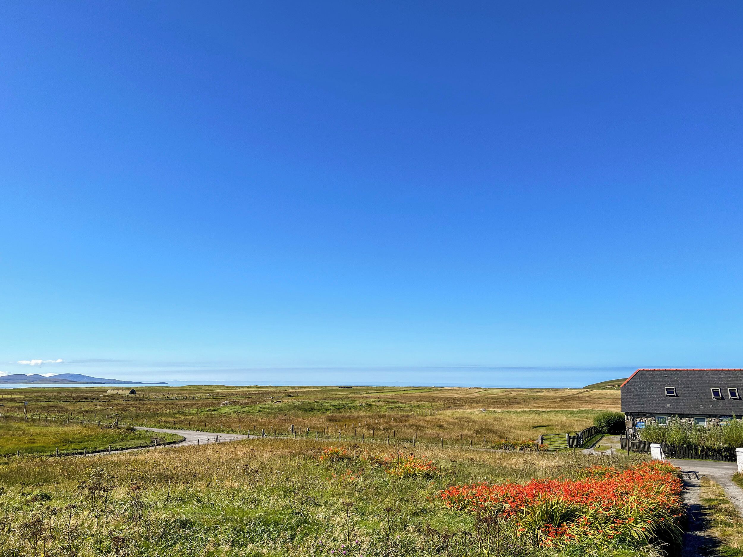 A rural landscape with a house, fields, and a clear sky.