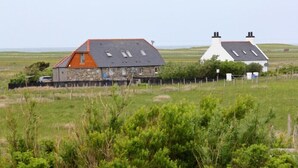 A stone house with a sloped roof and a fenced yard. - Kelp Cottage (South Uist)