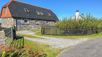 A stone building with a sloped roof, a wooden fence, and a gravel path leading to a gate.