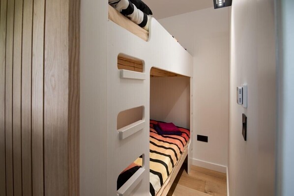 Habitación pequeña con literas, un estante y un termostato en la pared.