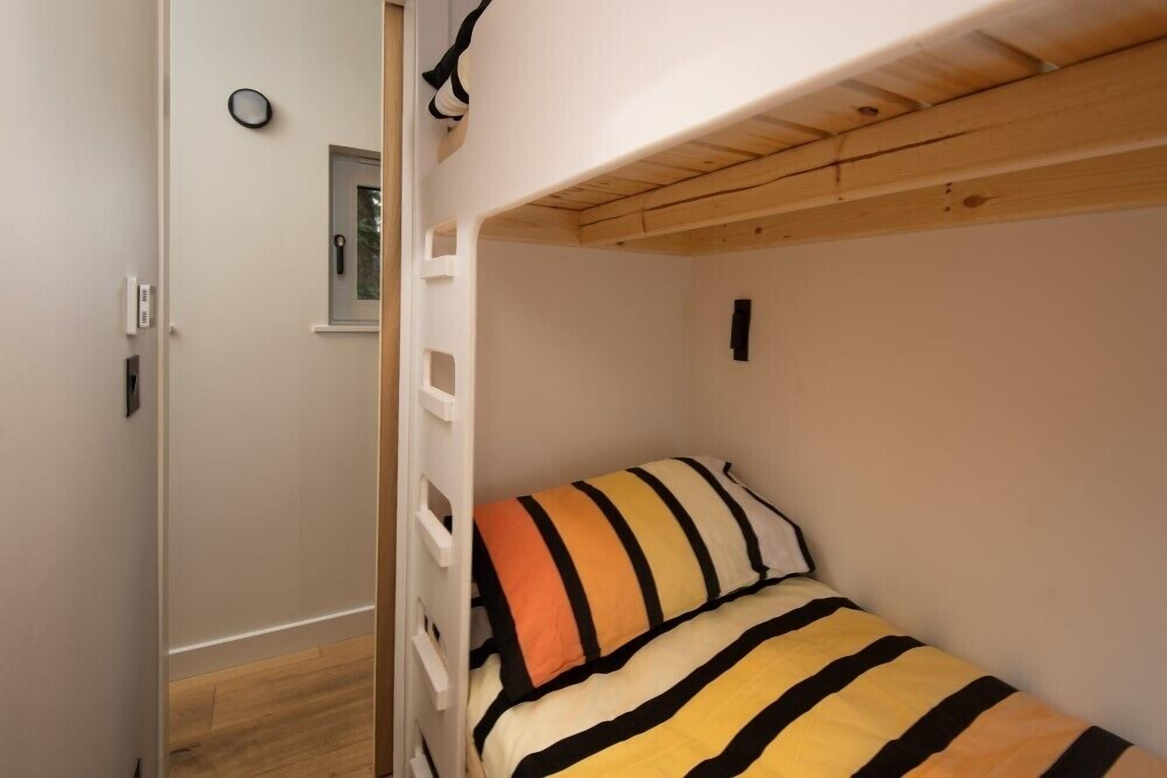 Una cama litera con un edredón a rayas, una ventana pequeña con vistas y una puerta con manija.