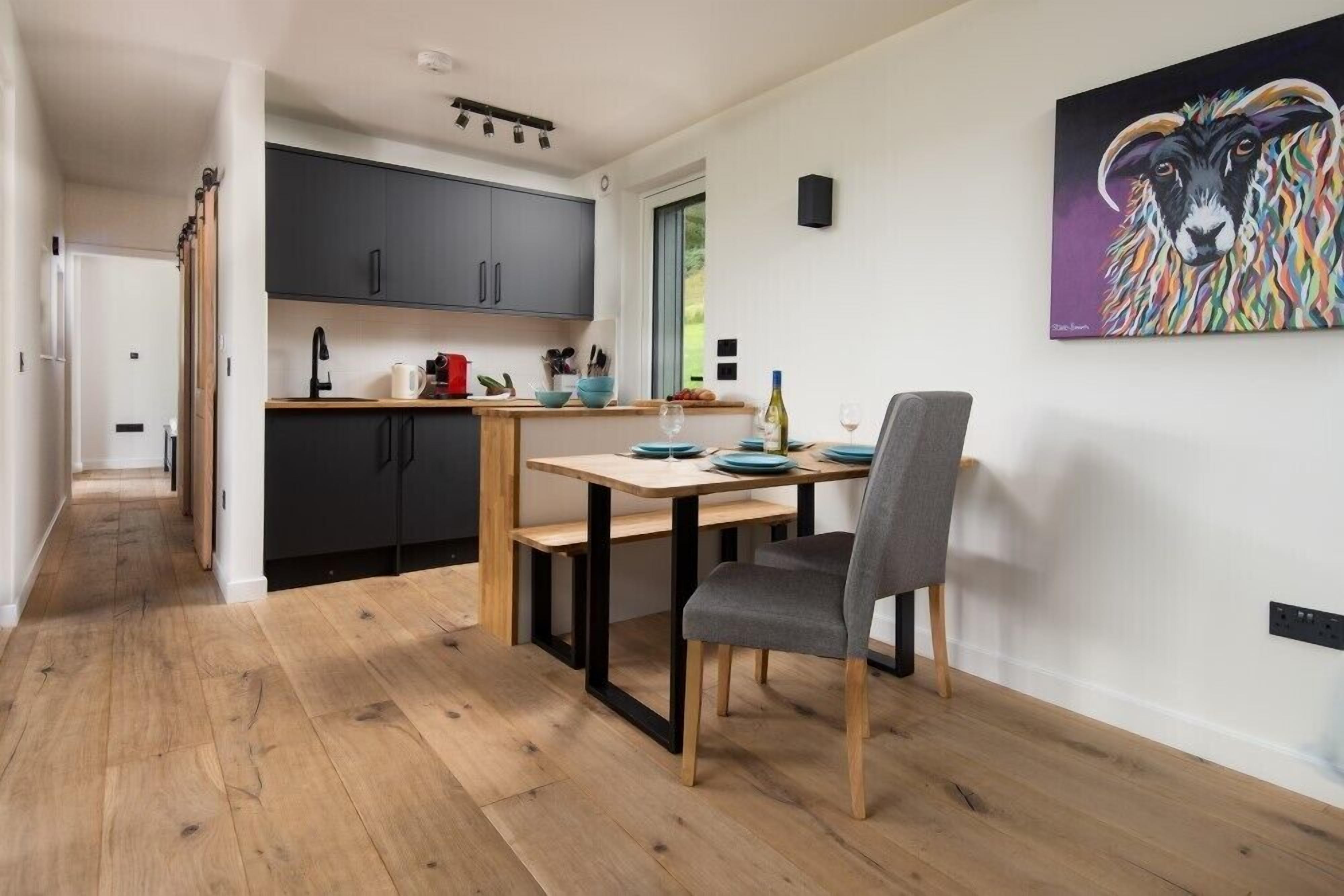 A modern kitchen with dark cabinets, a wooden countertop, and a dining area with a table and chairs.