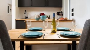 Una mesa de comedor dispuesta con platos azules, copas de vino y cubiertos, con una botella de vino en el centro.