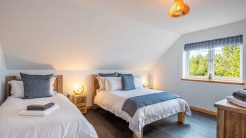 Quarto com duas camas, cabeceiras de madeira, mesas de cabeceira com luminárias, janela com vista para áreas verdes e luminária no teto.