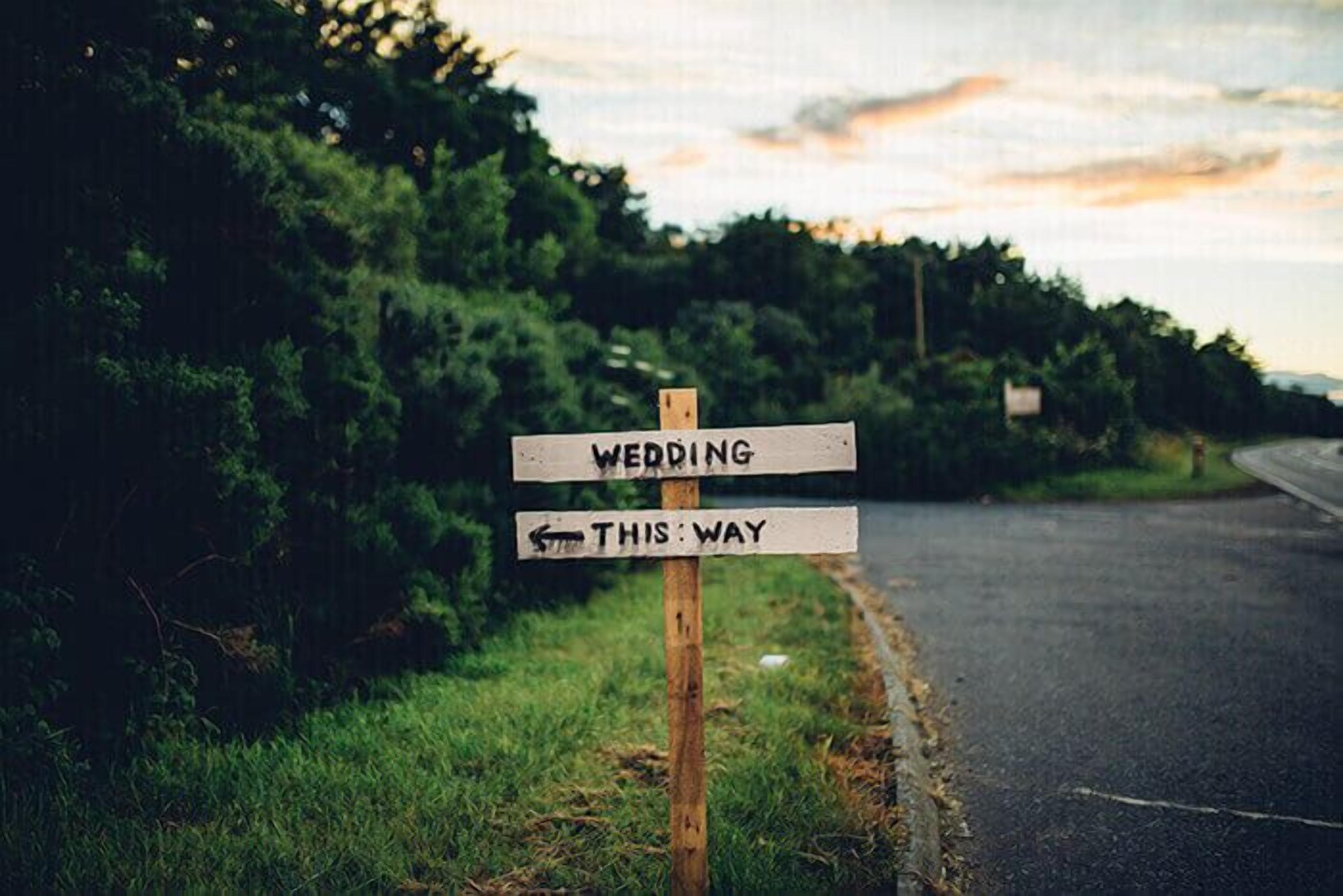 A wooden signpost with two directional signs, one pointing to the left and the other to the right, with the left sign indicating a wedding.