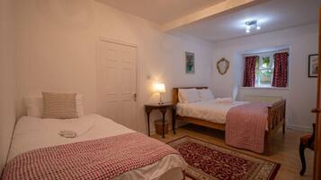 A bedroom with two single beds, a bedside table with a lamp, a window with curtains, and a door.