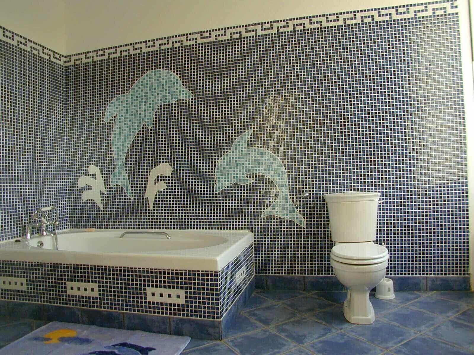 Un baño con un muro de mosaicos que muestra delfines, una bañera y un inodoro.