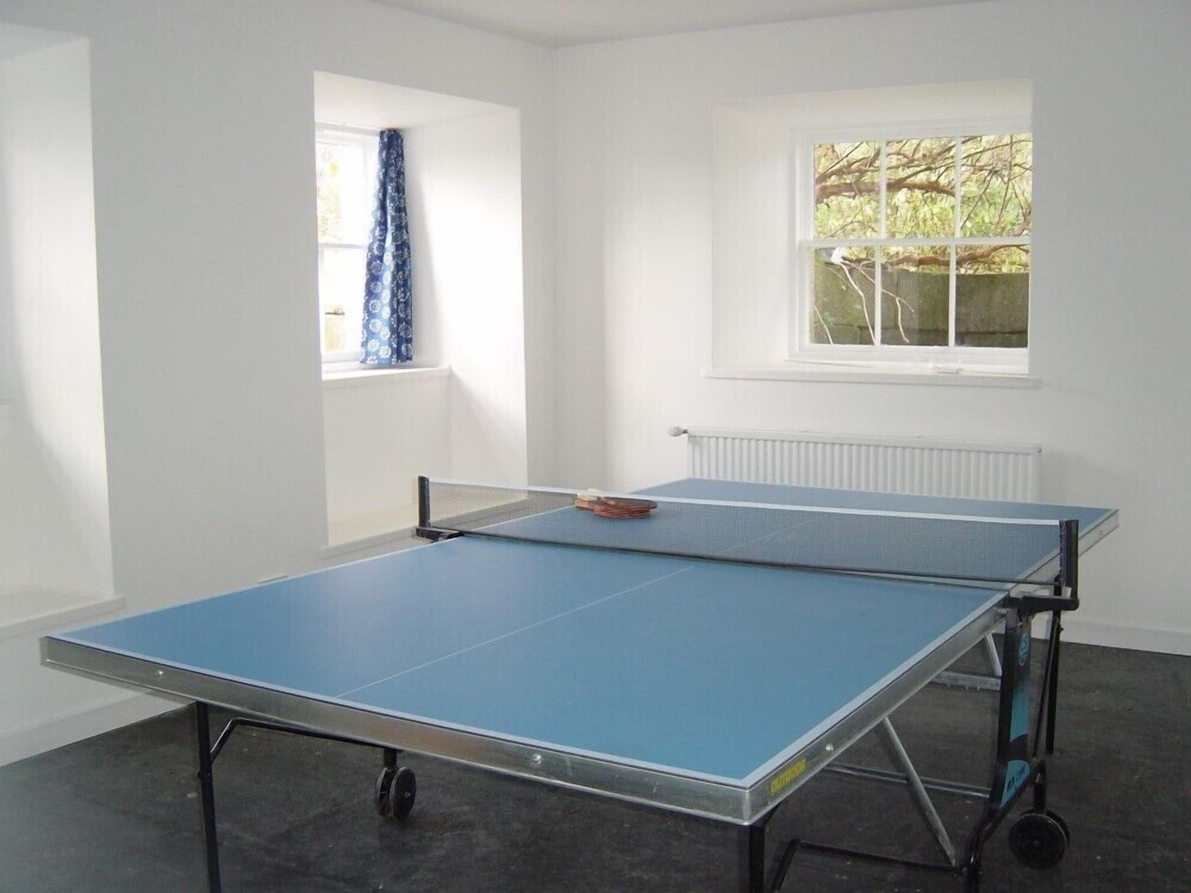 Una habitación con dos mesas de ping pong, un ventanal con cortina y un radiador.