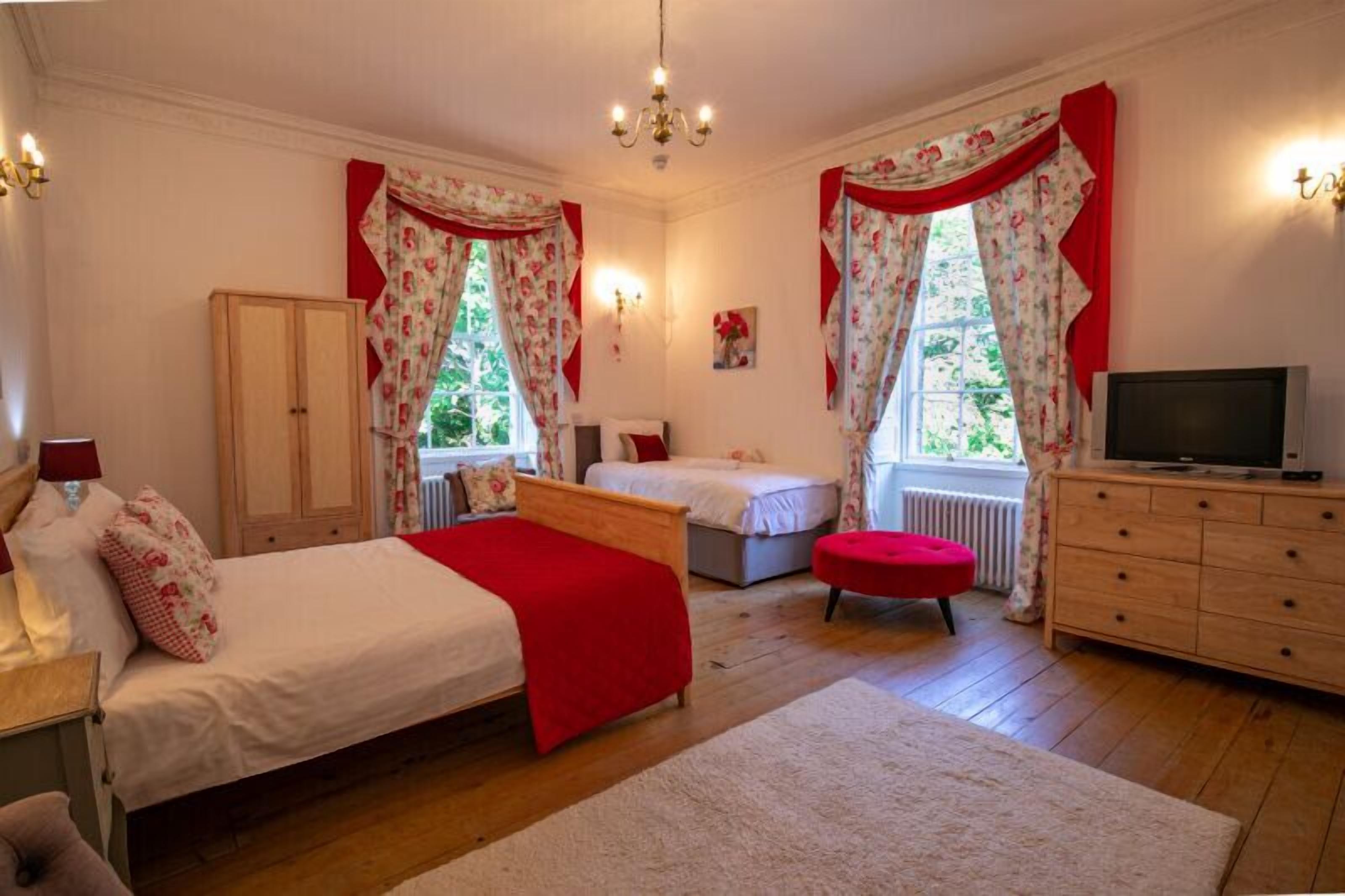 A bedroom with two beds, a dresser, a TV, and a window with curtains.
