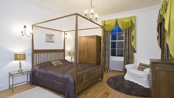 A four-poster bed with a wooden frame, a white radiator, a white armchair, and a small table with a lamp.