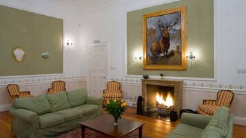 Ein Wohnzimmer mit Kamin, grünen Sofas, gestreiften Sesseln und einem Bild von einem Reh.