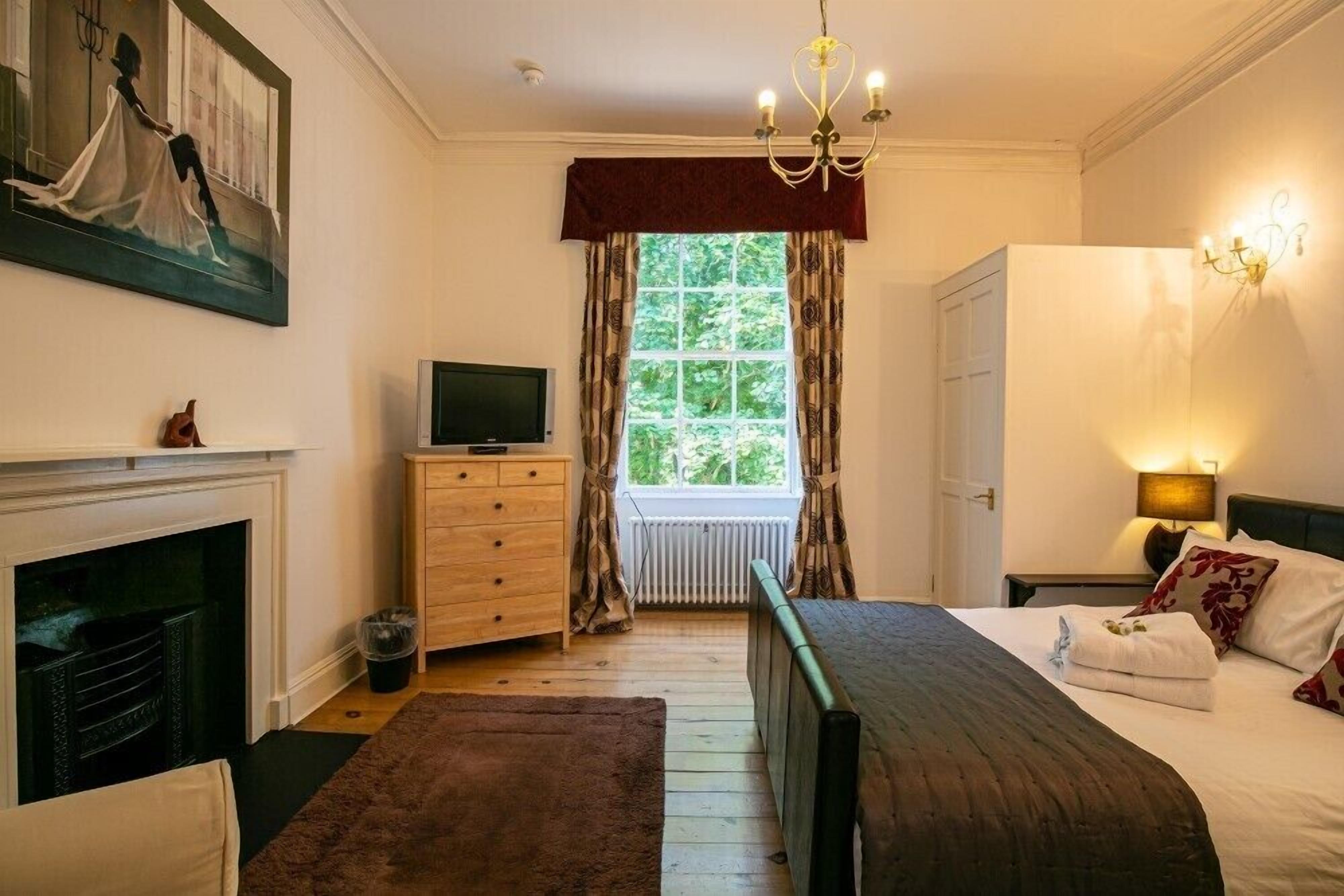 Un dormitorio con cama, televisor, chimenea y ventana con cortinas.