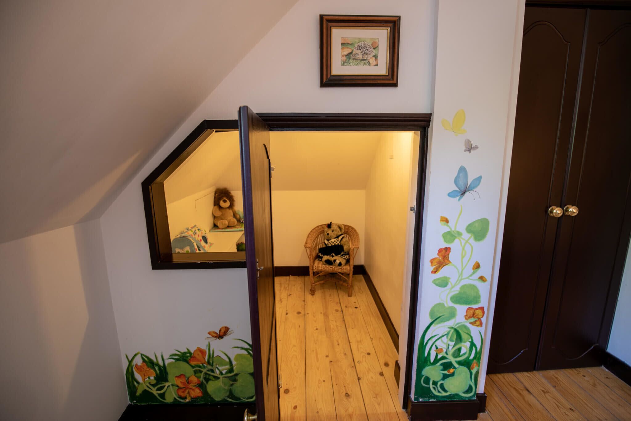 Una escalera con piso de madera que lleva a una habitación con una silla de mimbre y un osito de peluche.