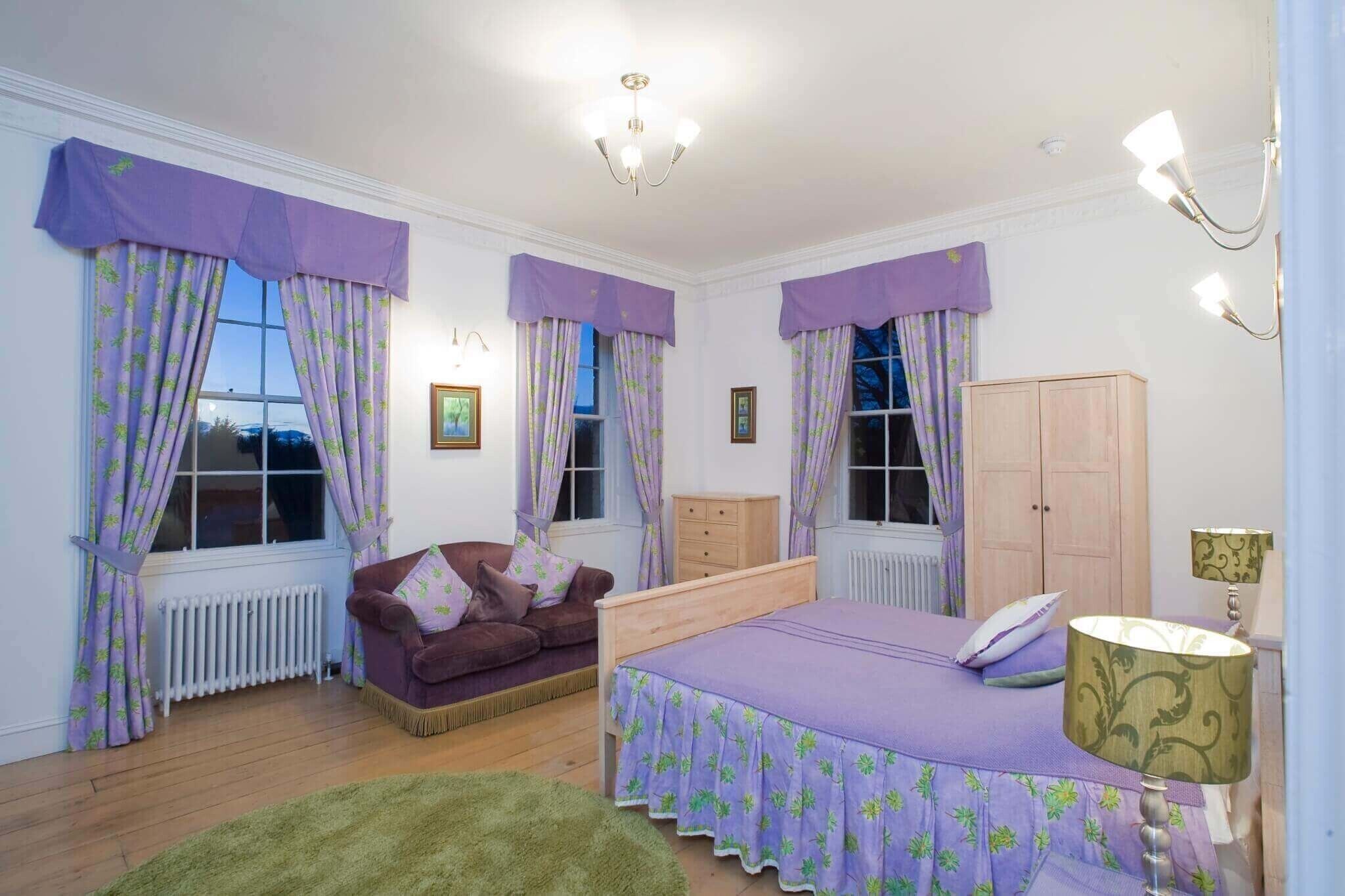 Un dormitorio con cama, armario de madera, cómoda, sofá púrpura y alfombra verde.