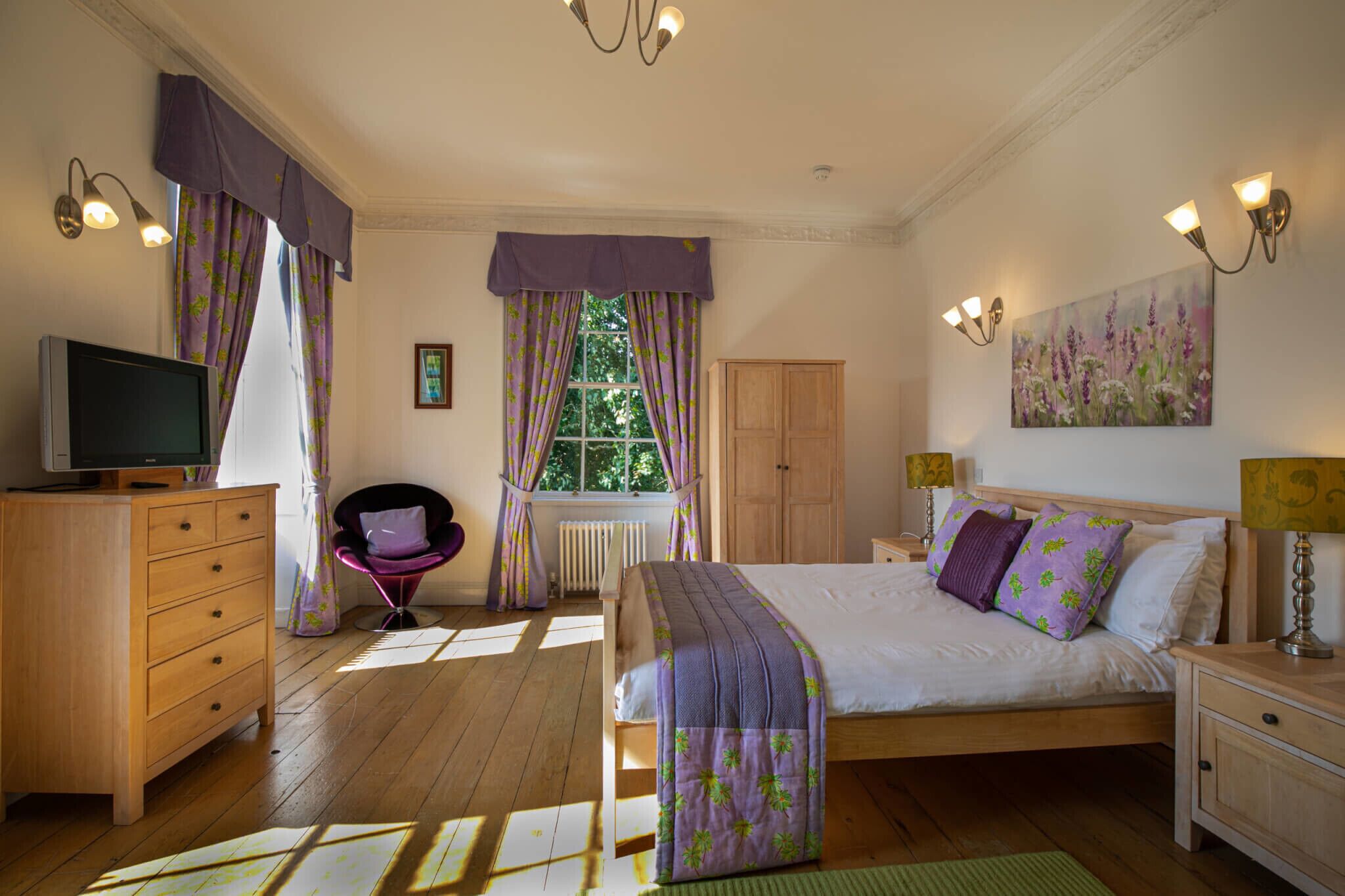 A bedroom with a bed, wooden dresser, chair, and a painting on the wall.