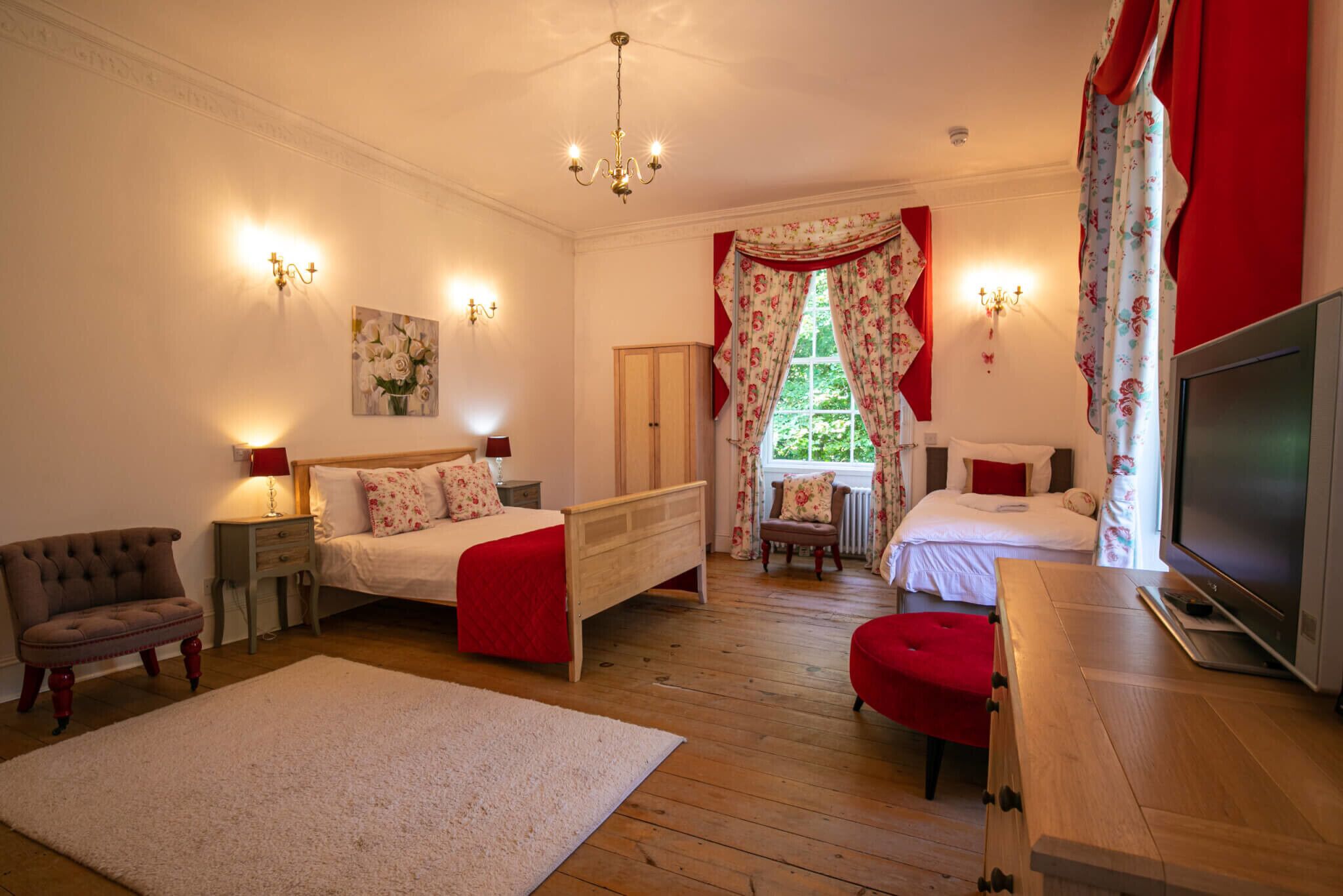 Quarto com duas camas, televisão e piso de madeira.