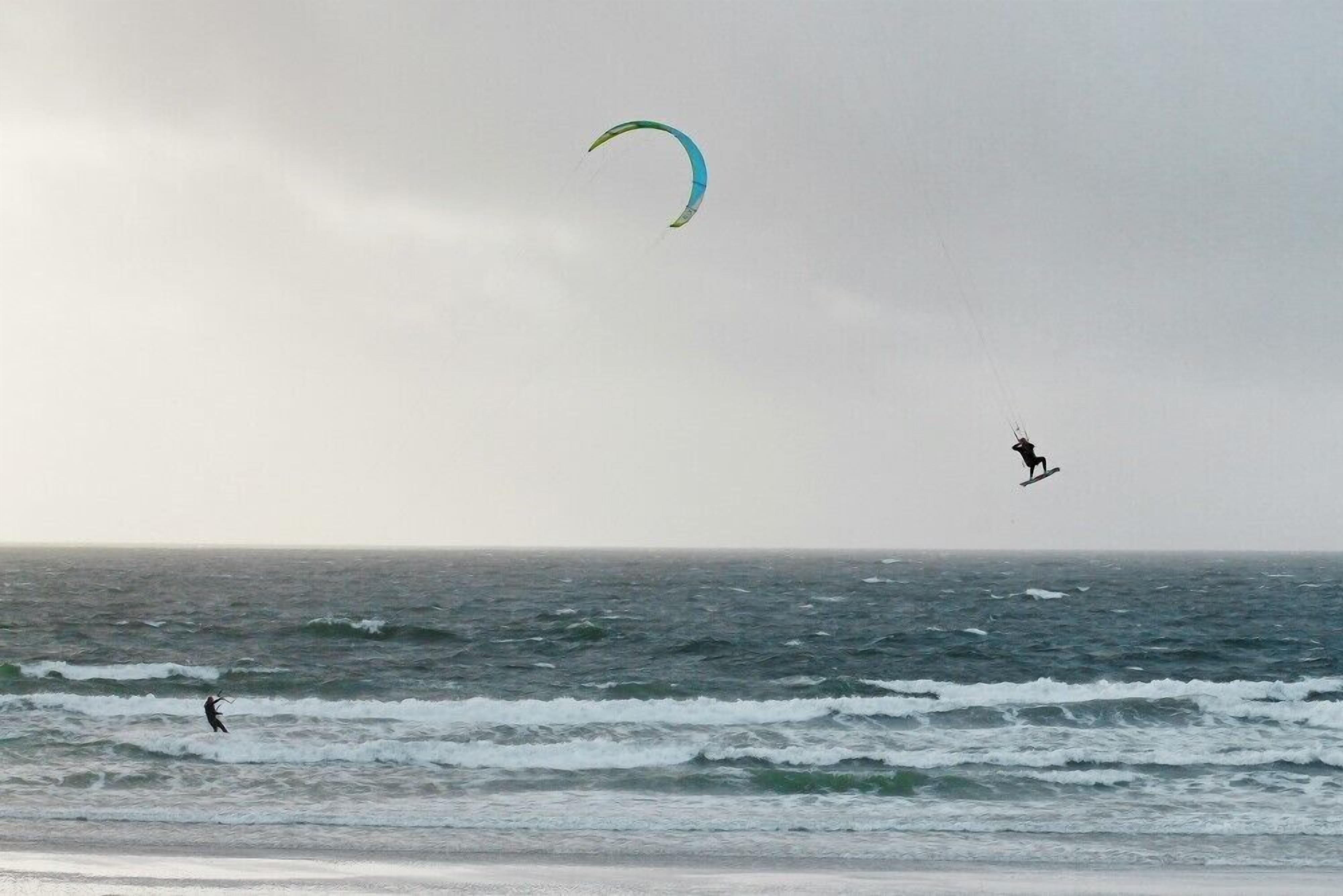 A beach with waves and a person kite surfing.