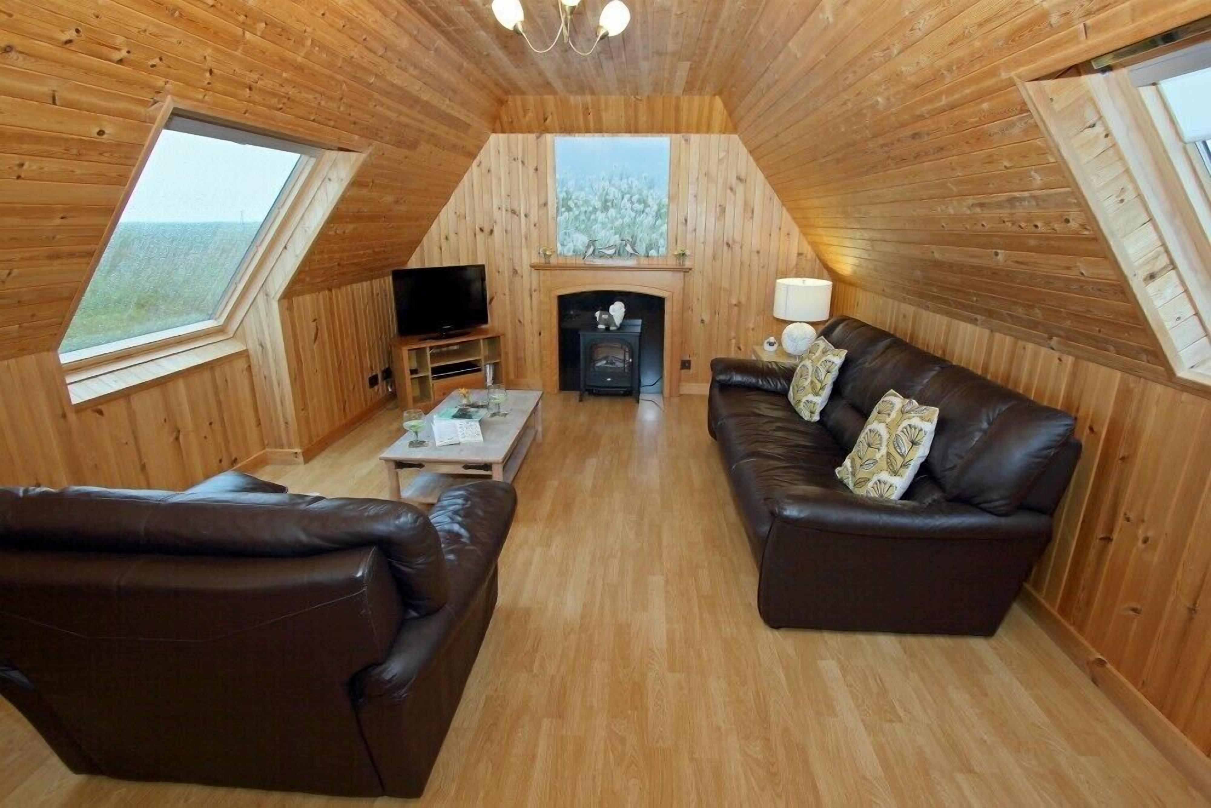 Un interior acogedor de madera con chimenea, sofás de cuero y televisor.