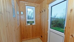 A wooden-paneled hallway with a small window, a door, and a view of a garden. - Canach Cottage (South Uist)