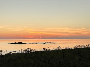 A coastal landscape at sunset with a clear sky, calm sea, and rocky outcrops. - Canach Cottage (South Uist)