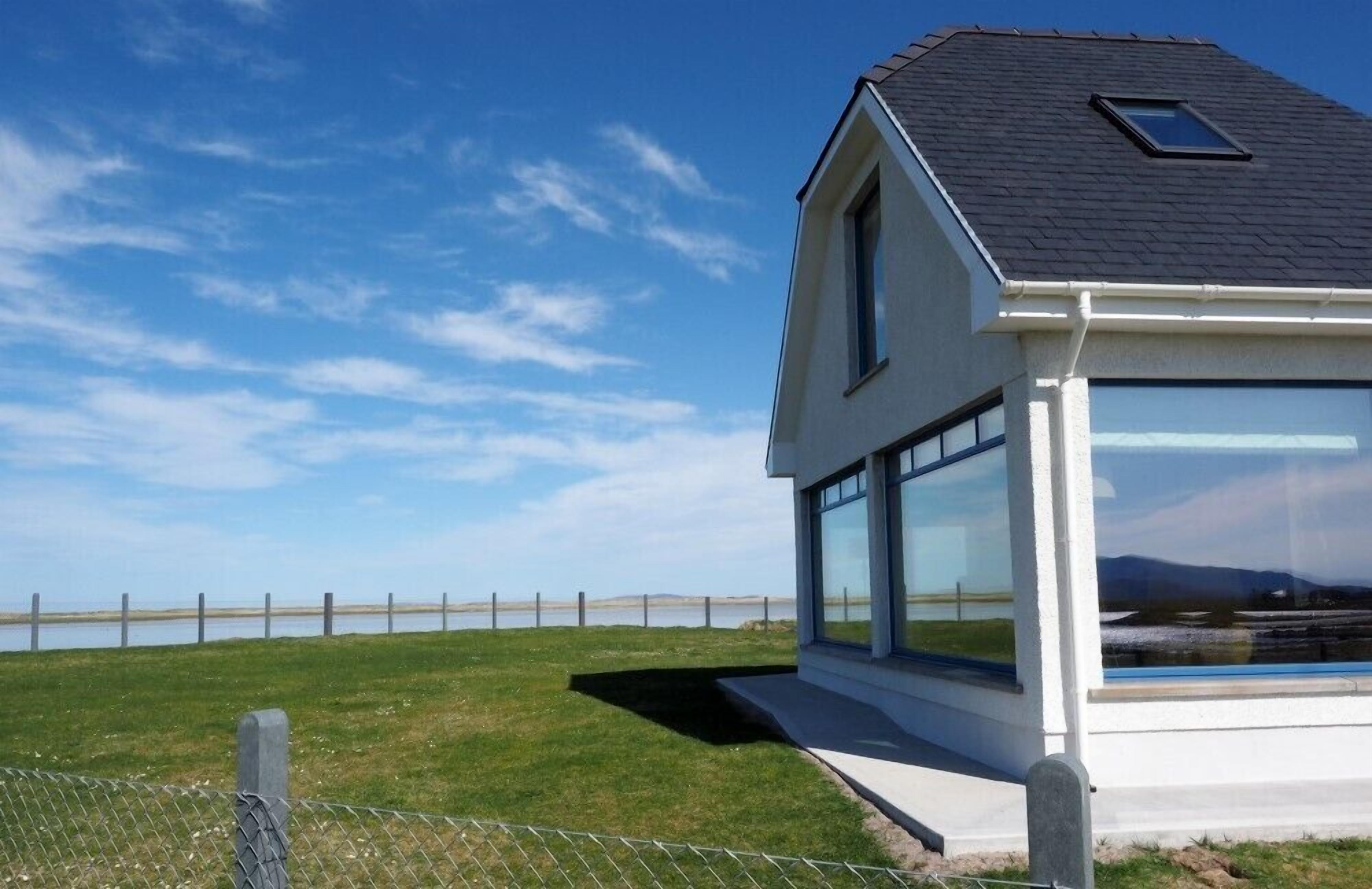 Une maison moderne dotée de grandes fenêtres et d’un toit en pente, située au bord d’un plan d’eau.