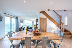 A spacious dining area with a wooden table, metal chairs, a fruit bowl, and a bottle of wine.