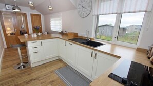 A modern kitchen with white cabinets, a black stove, and a window with a view of the outside. - Tulloch House (South Uist)