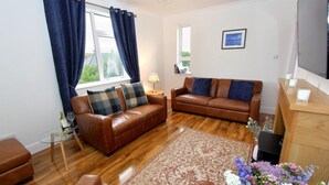 A living room with two leather sofas, a glass coffee table, a patterned rug, and a wooden sideboard. - Tulloch House (South Uist)