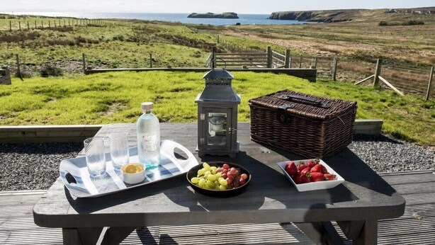 Tavolo da picnic con cibo e una lanterna su una terrazza con vista sul paesaggio costiero.