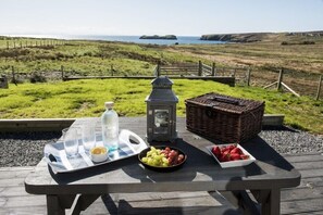 Un montaje para picnic con una mesa, comida y un farol sobre una terraza con vistas al paisaje costero.
