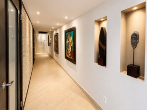 Un couloir aux murs ornés d’œuvres d’art, avec un plancher en bois et une porte sur le côté gauche.