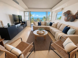 A modern living room with a large sofa, a coffee table, and wicker chairs.