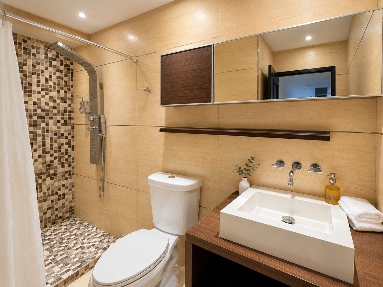 A bathroom with a shower, toilet, sink, and a mirror above the sink.