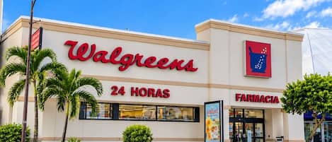 Una farmacia Walgreens con un letrero que indica servicio 24 horas, palmeras y un cielo azul despejado.