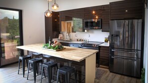 Een moderne keuken met donker houten kastjes, roestvrijstalen apparatuur, een houten kookeiland met barkrukken en hanglampen.