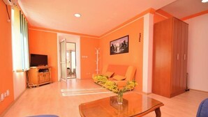 Un salon aux murs orange, avec une table basse en bois, un canapé et un téléviseur.