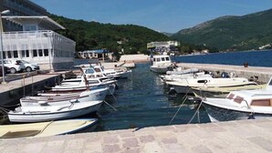 Un port de plaisance où sont amarrés plusieurs bateaux, un bâtiment doté d’un toit en pente et un paysage montagneux en arrière-plan.