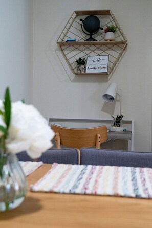 A modern living room with a hexagonal wooden shelf displaying a globe, a potted plant, and a sign with wifi details. A wooden chair and a small table with a lamp and a pen holder are visible. - Pet-Friendly Cottage Near Airport (North Charleston)