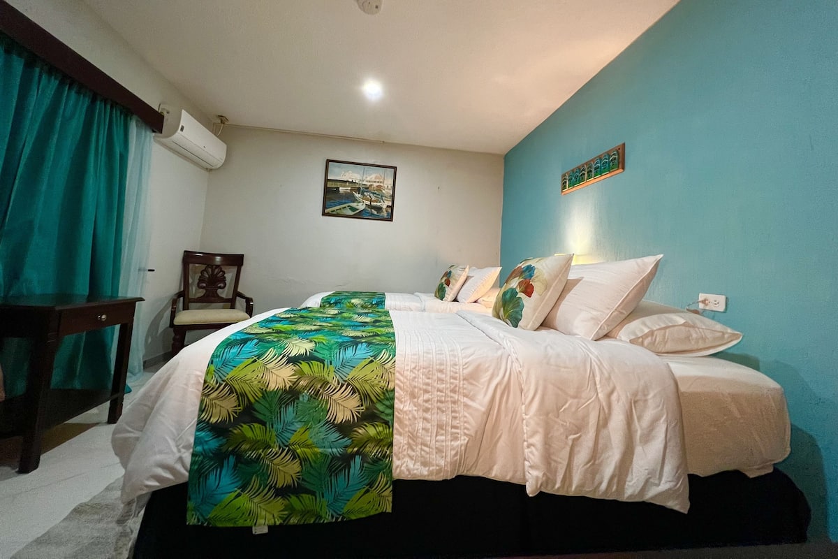 A bedroom with a bed, a chair, a painting, and a wall-mounted air conditioning unit.
