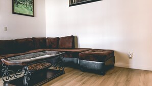 Un salon avec un canapé en cuir marron, une table basse en verre et deux tableaux accrochés au mur.