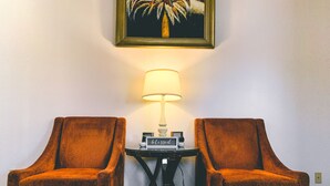 Une pièce comprenant deux fauteuils, une petite table avec une lampe et un tableau encadré accroché au mur.