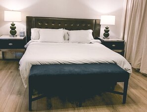 Relax in a spacious room with a large bed, bedside tables, and a comfortable bench.