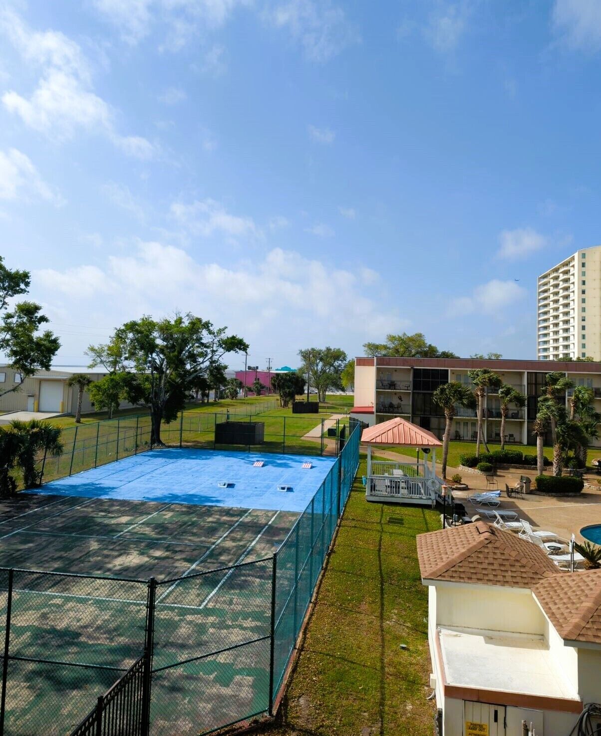 A residential area with a fenced tennis court, a covered seating area, and a tall building in the background.