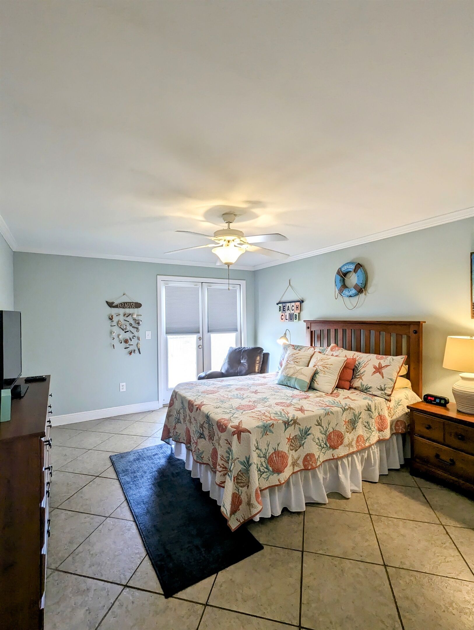A bedroom with a bed, a ceiling fan, a nightstand, a dresser, and a television.