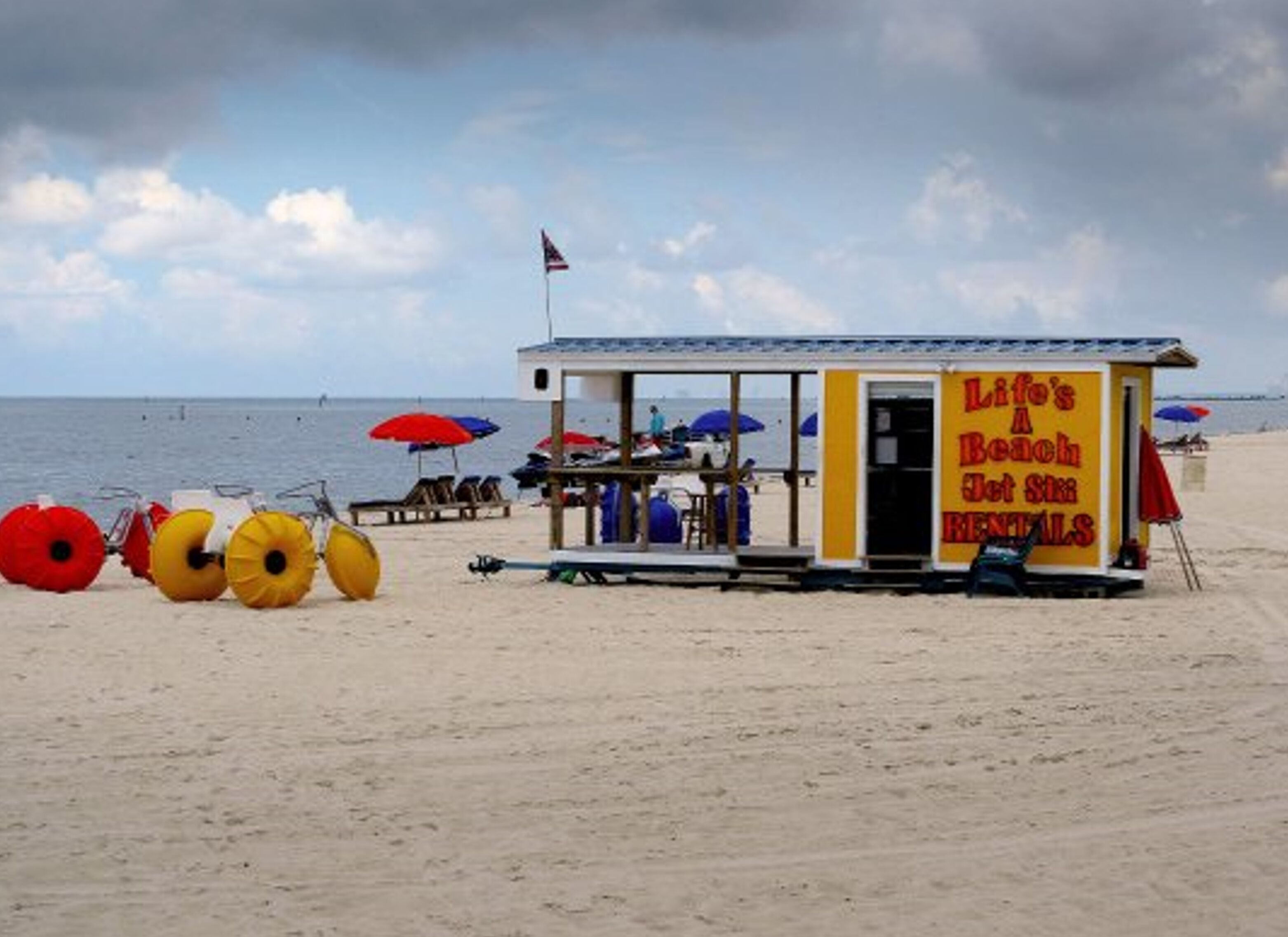 A beachside kiosk named "Life's a Beach Get Sick Rentals" with beach chairs and umbrellas.