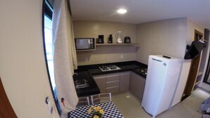 Una cucina compatta con forno a microonde, fornello e frigorifero. C'è un tavolino con tovaglia a quadri e un vaso con fiori.