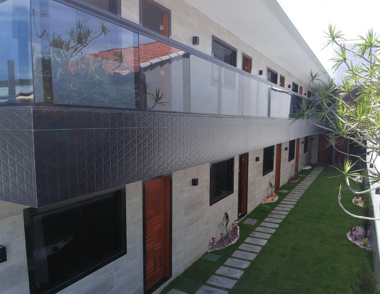 A modern building with a glass balcony, a tiled exterior, and a small garden with a lawn and stepping stones.
