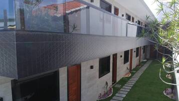 A modern building with a glass balcony, a tiled exterior, and a small garden with a lawn and stepping stones.