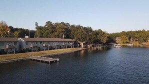 A waterfront property with a dock, a row of single-story buildings, and a forested hill in the background. - Adorable Lake Getaway (Hot Springs)