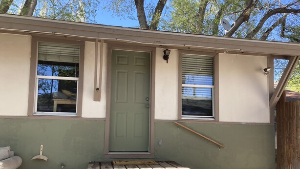 A single-story building with a green door, two windows with blinds, a small porch with a wooden bench, and a satellite dish on the roof. - Private 1br near downtown Flagstaff, NAU, Hospital (Flagstaff)